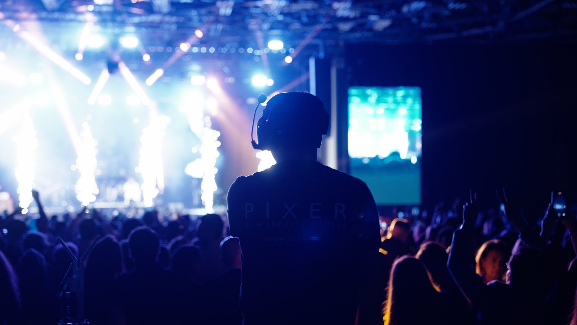 Pixer team member silhouette facing a packed concert stage with dramatic blue and white lighting